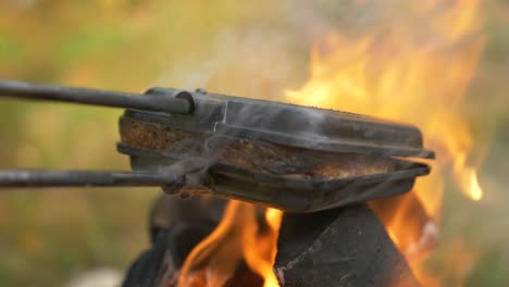 close up shot of square sandwich pie iron cast, grilling cheese sandwich over hot campfire