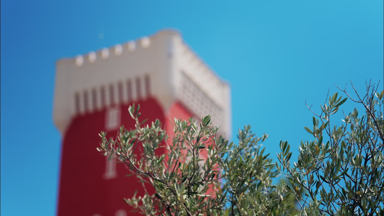 Green tree moving in the wind near the red tower of the Cremat Castle Winery over blue sky