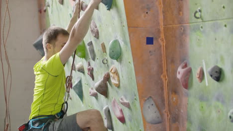 portrait of a climber preparing to climb the wall in the hall to chalk his hands and climb the wall with insurance in slow motion.