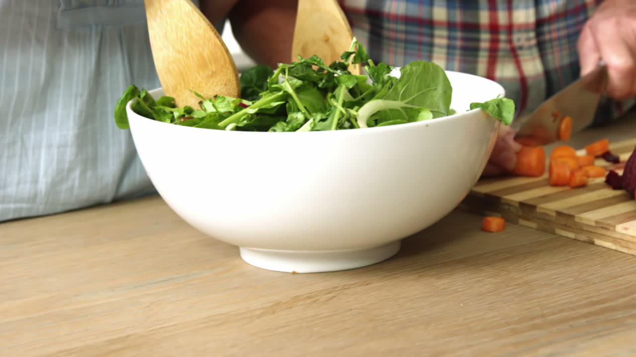 una pareja lanzando una ensalada en la cocina.