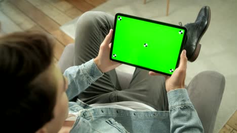 vista desde el hombro de un hombre sosteniendo y usando gestos con las manos en una pantalla de maqueta verde, una tableta digital sentada en una silla, un hombre comprando cosas o navegando por internet