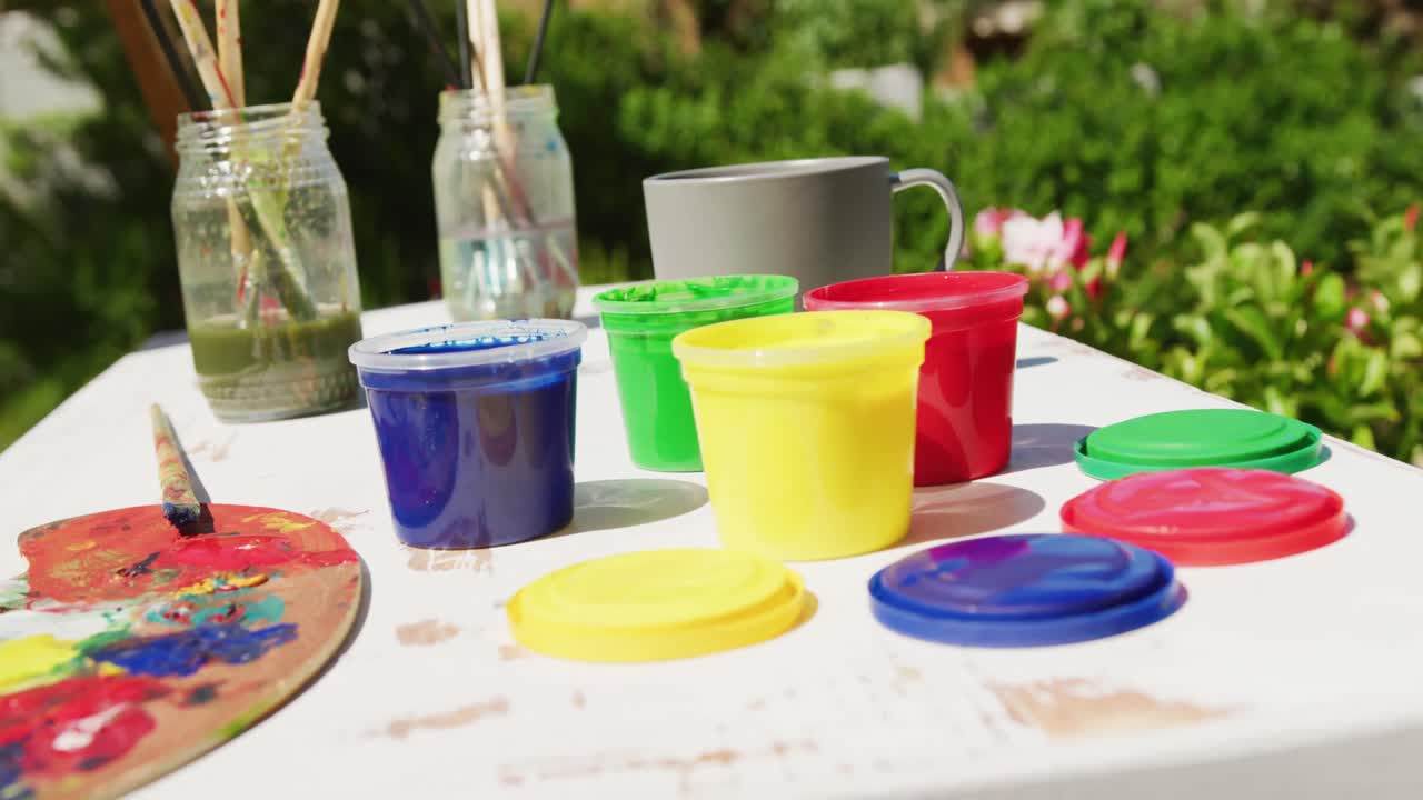 Close up of colourful paints and painting equipment lying on table in garden