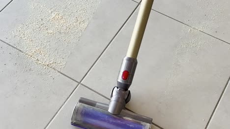 a cordless vacuum cleaner removes scattered crumbs from a light-colored tiled floor. bright natural lighting highlights the cleaning process with smooth, steady camera movement