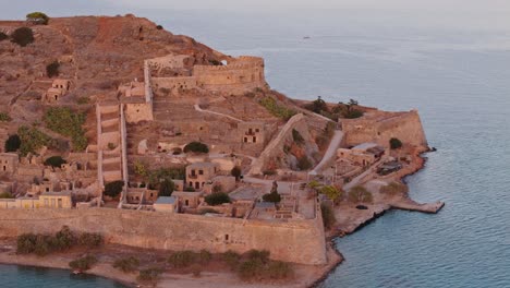 Aerial-orbit-of-Spinalogka-fortress-ruins-at-golden-hour-soft-light-glow-spreads-across-walls