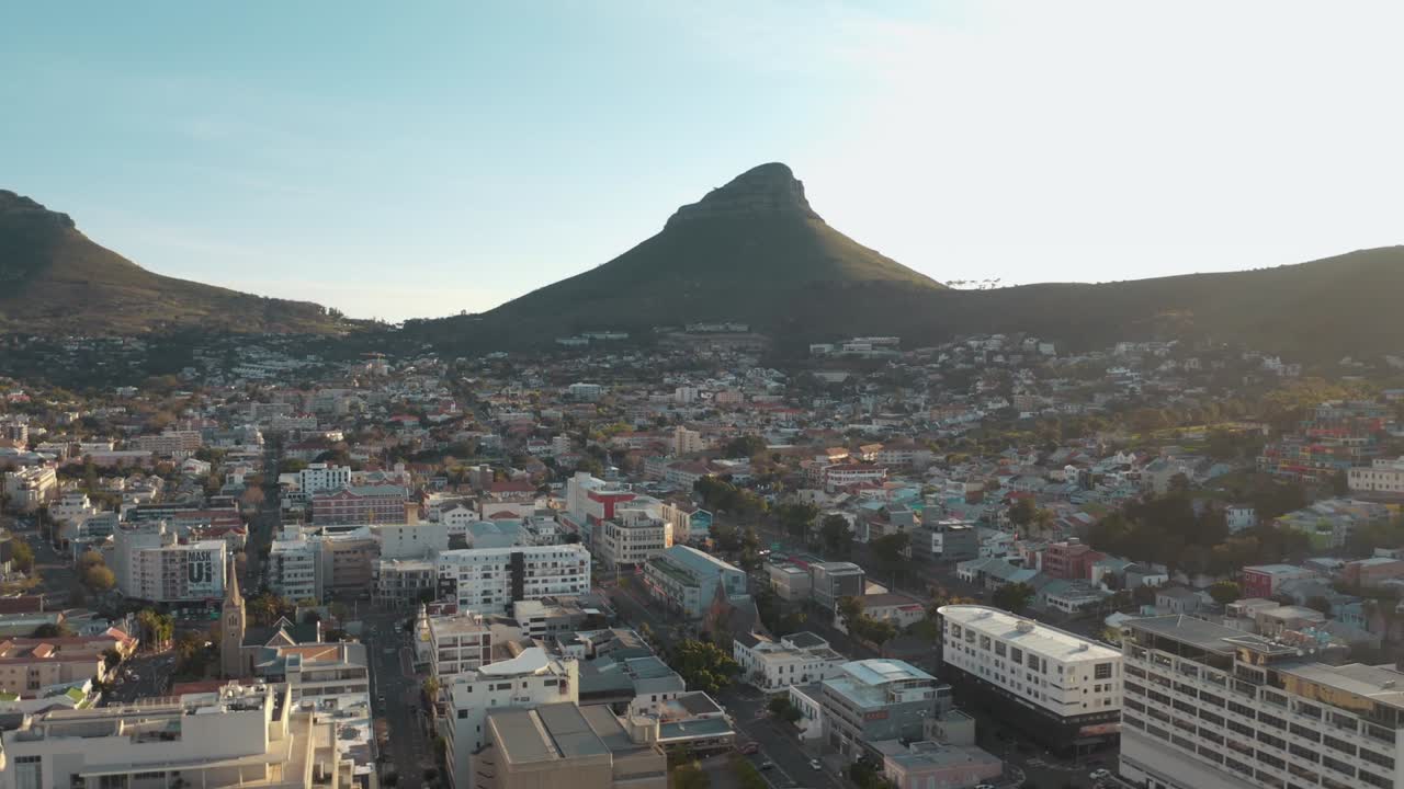 Aerial drone view showcases crowded cityscape nestled beside majestic arid mountains under clear blue sky in Iceland. The rugged mountain terrain contrasts with the dense urban sprawl below