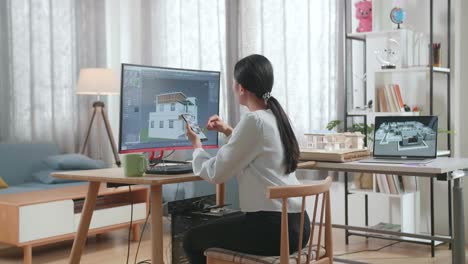 asian woman engineer using smartphone while designing house on a desktop at home. cyber games house design and decoration
