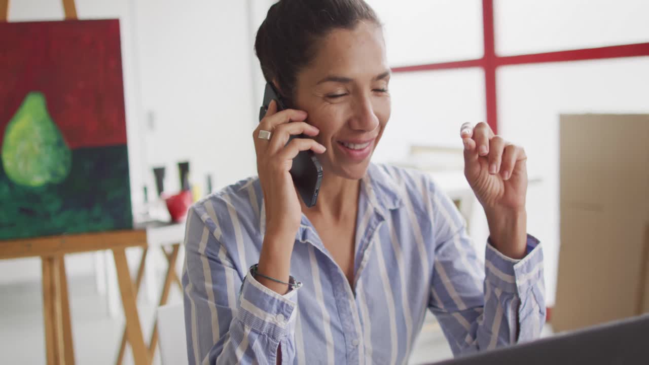 video de una feliz diseñadora biracial usando un teléfono inteligente en el estudio
