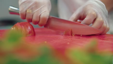 cook cuts a fresh tomato for a salad with a knife