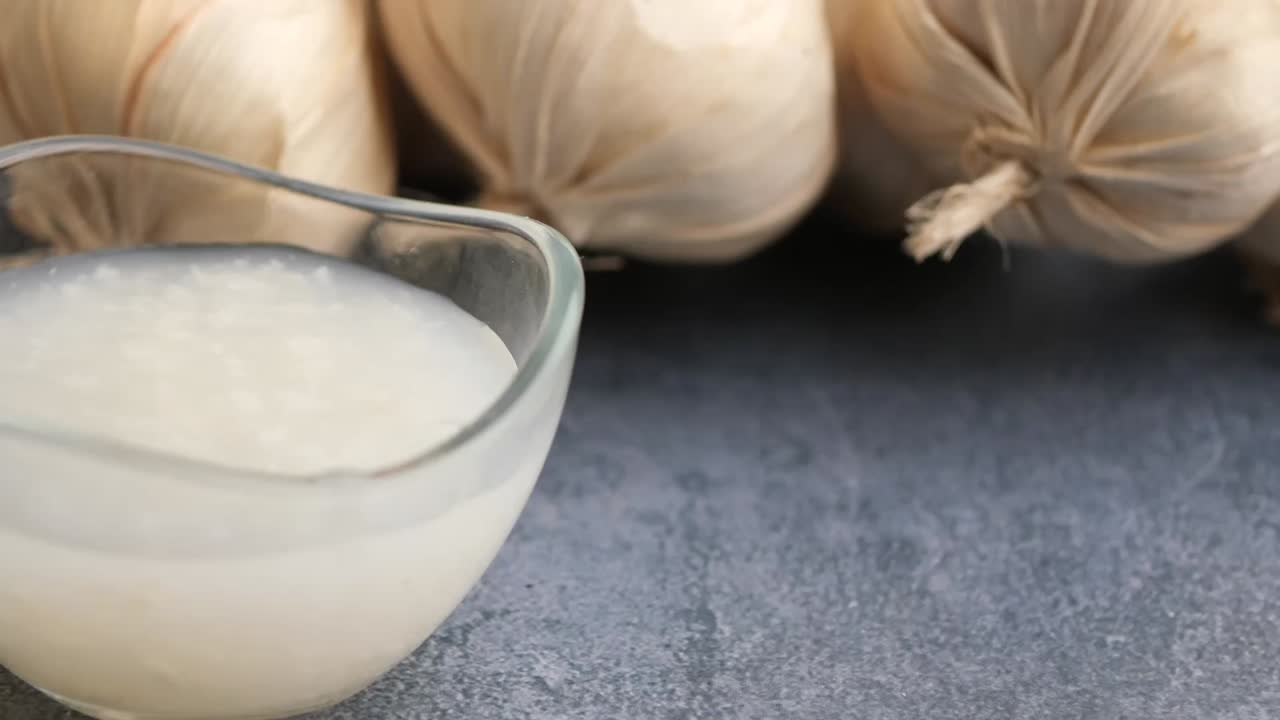 Garlic juice in glass bowl with garlic bulbs in background