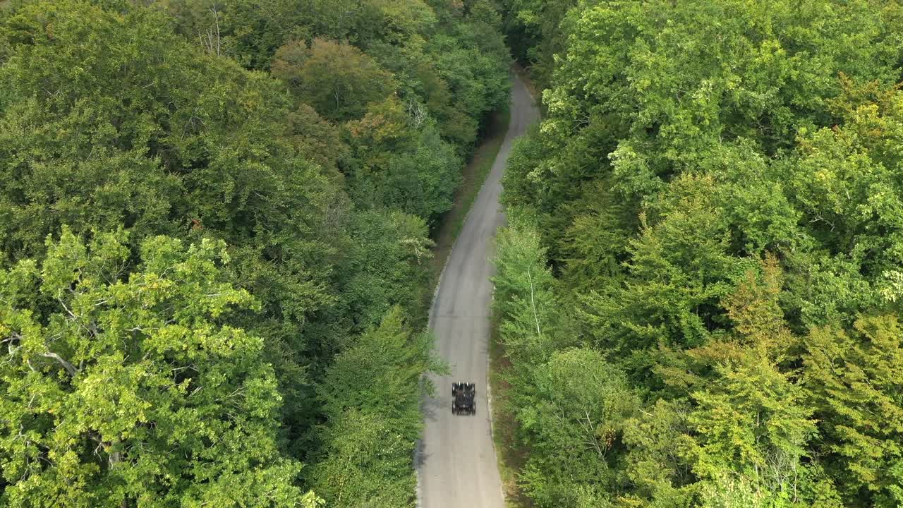 Aerial view of dark car driving on secluded road through dense green forest, Oise, France