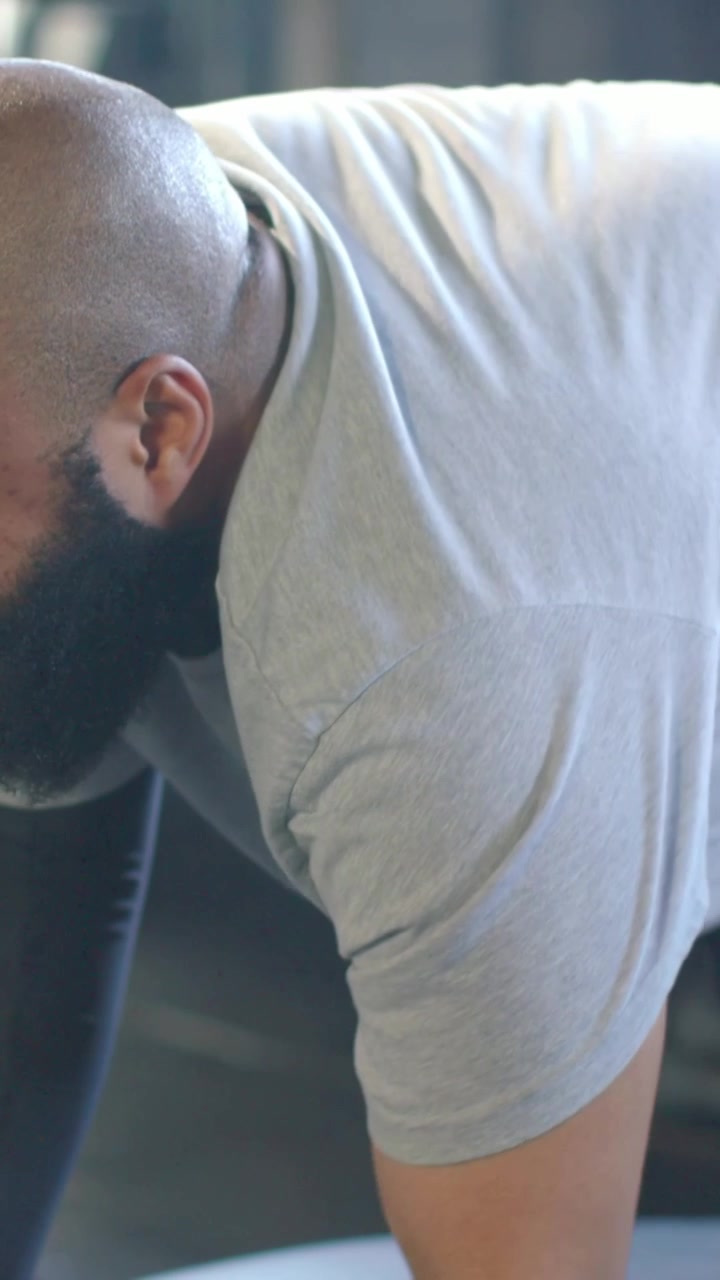 Vertical video: Gripping dumbbell man in gray tee using bench doing one-arm row at gym for strength