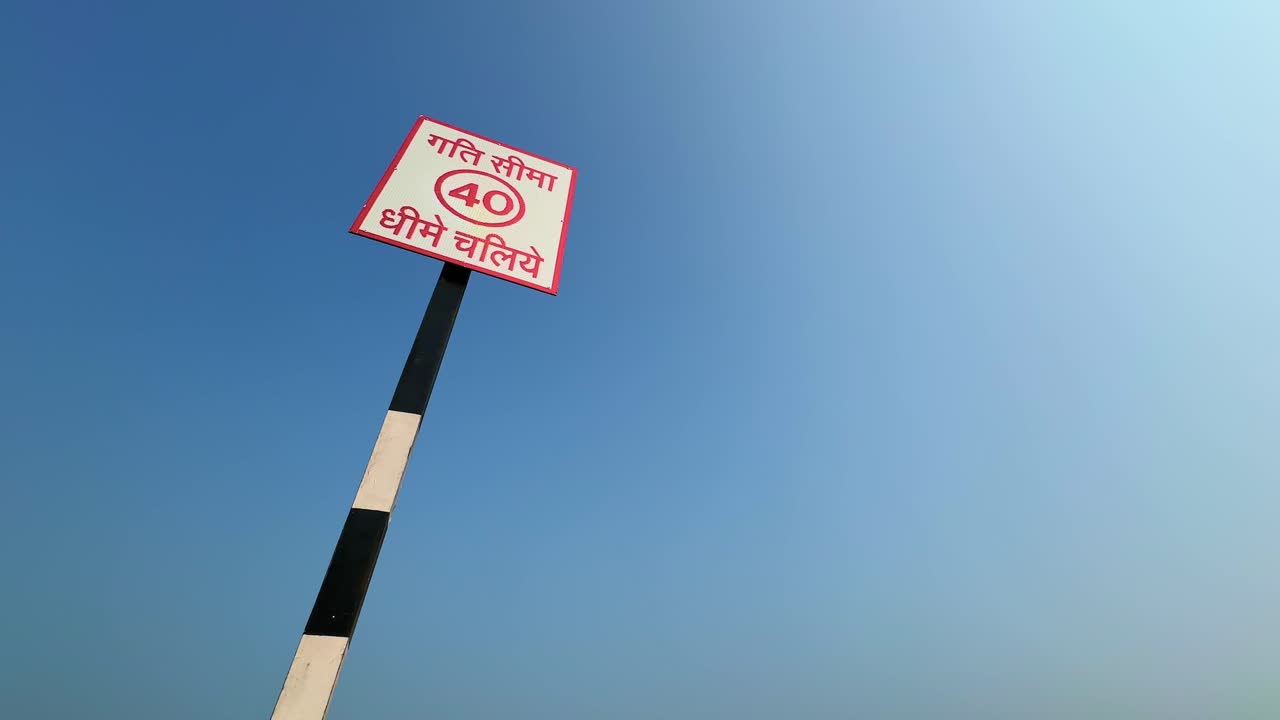 A smooth slow tracking shot featuring an Indian road sign that reads “Speed Limit 40 – Drive Slowly” in Hindi, captured under a clear blue sky, emphasizing traffic awareness and road safety
