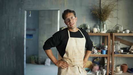 joven alfarero feliz con gafas se limpia las manos en su delantal y posa para la cámara. retrato de un joven artista. tradicional