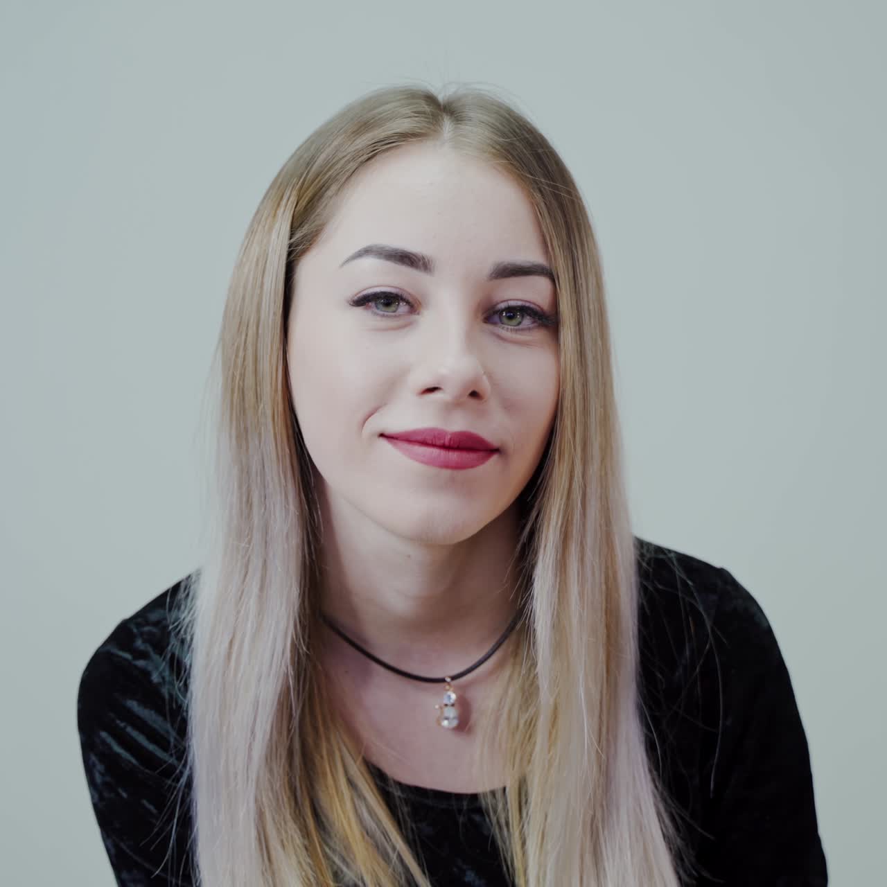 Beautiful blonde girl on white background sitting on white background smiling. Video in a studio.