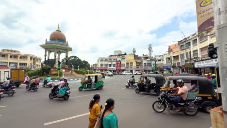 vibrant downtown mysuru in karnataka, showcasing bustling streets with auto-rickshaws, scooters, and pedestrians around a historic roundabout. captures daily life and urban charm in south india.