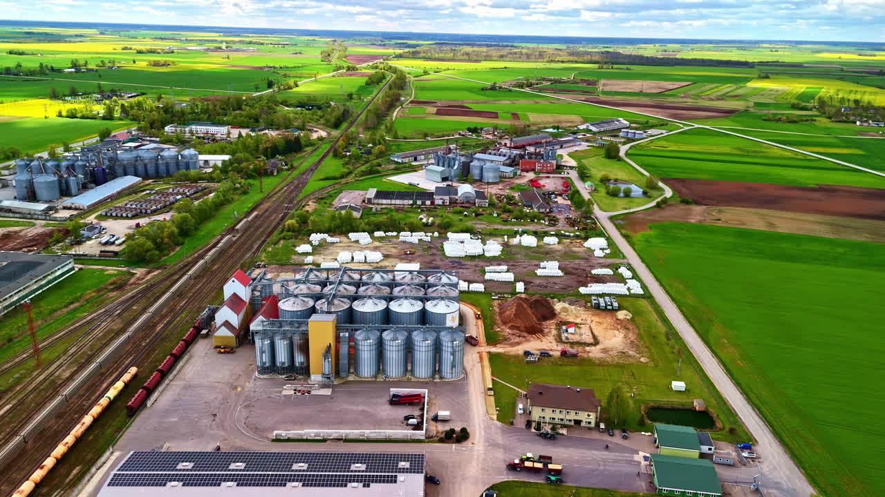 Silos and train track converge near field edge with metal structure and waste below