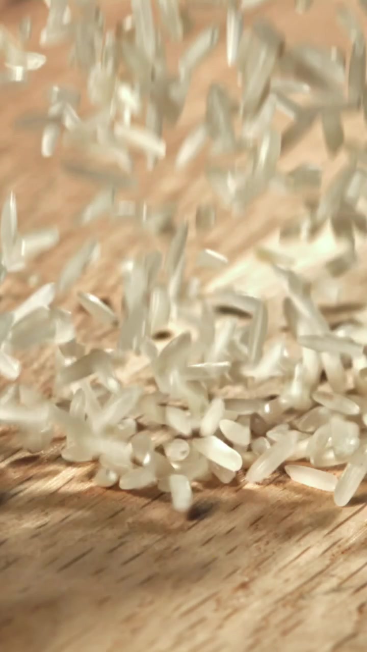 Raw White Rice Grains Falling onto a Wooden Surface