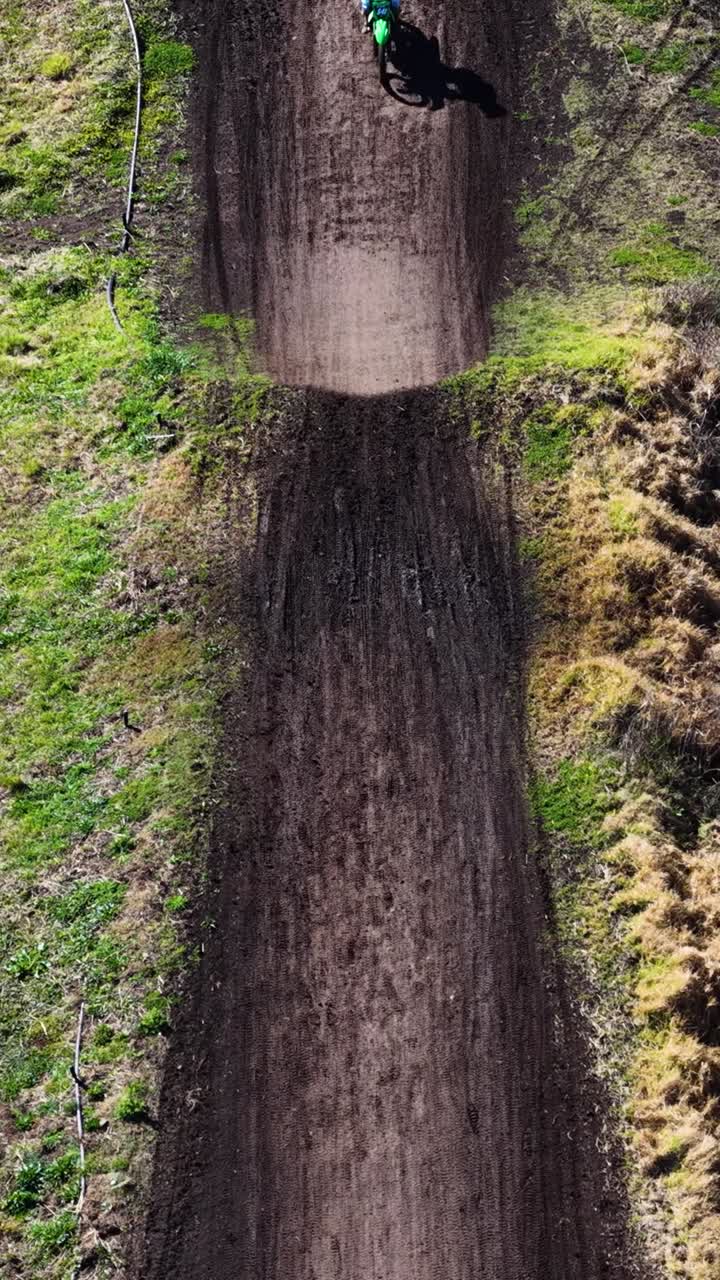 Prospettiva verticale dall'alto di moto da cross che gareggiano lungo una stretta pista sterrata rurale.