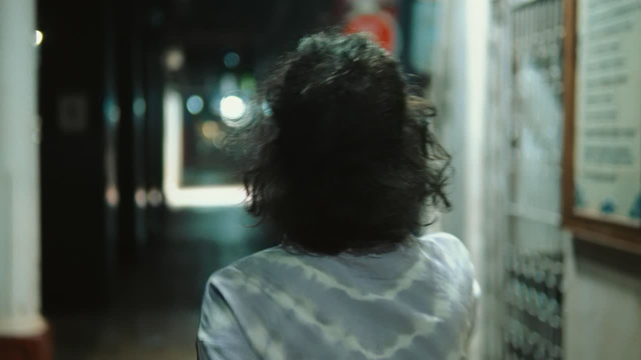 Young person briskly walking through a dimly lit urban alley at night, creating a sense of urgency or escape