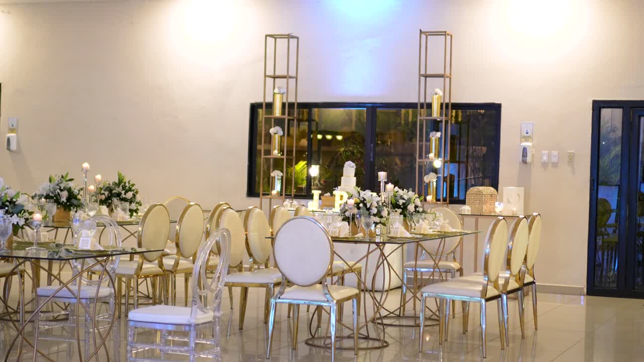 sala de reuniones decorada para una boda, con mesas de vidrio con piezas centrales de follaje y elegantes sillas doradas