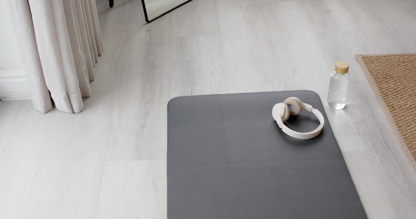 Camera is recording dark gray mat with beige headphones resting, showing prepared workout corner