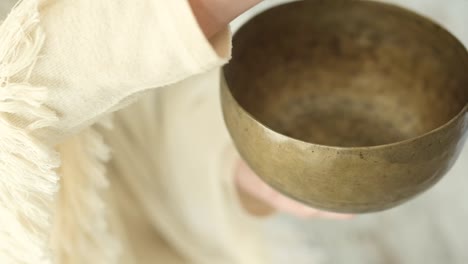 Woman-playing-bowl-gong-with-mallet-against-fireplace