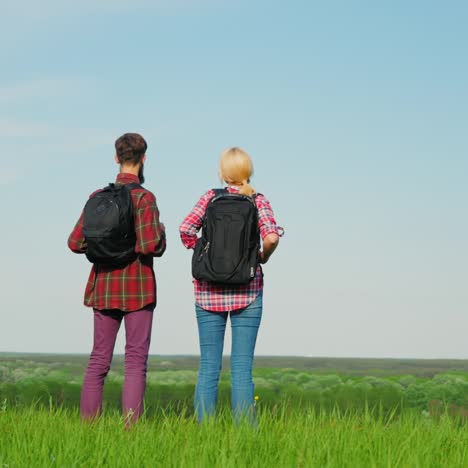 a couple of tourists with backpacks are walking along the crest of a large green hill 1