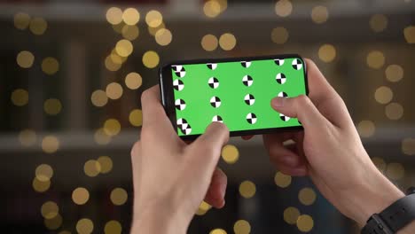 closeup view of smartphone with green screen and tracking markers in man hands on a bokeh background