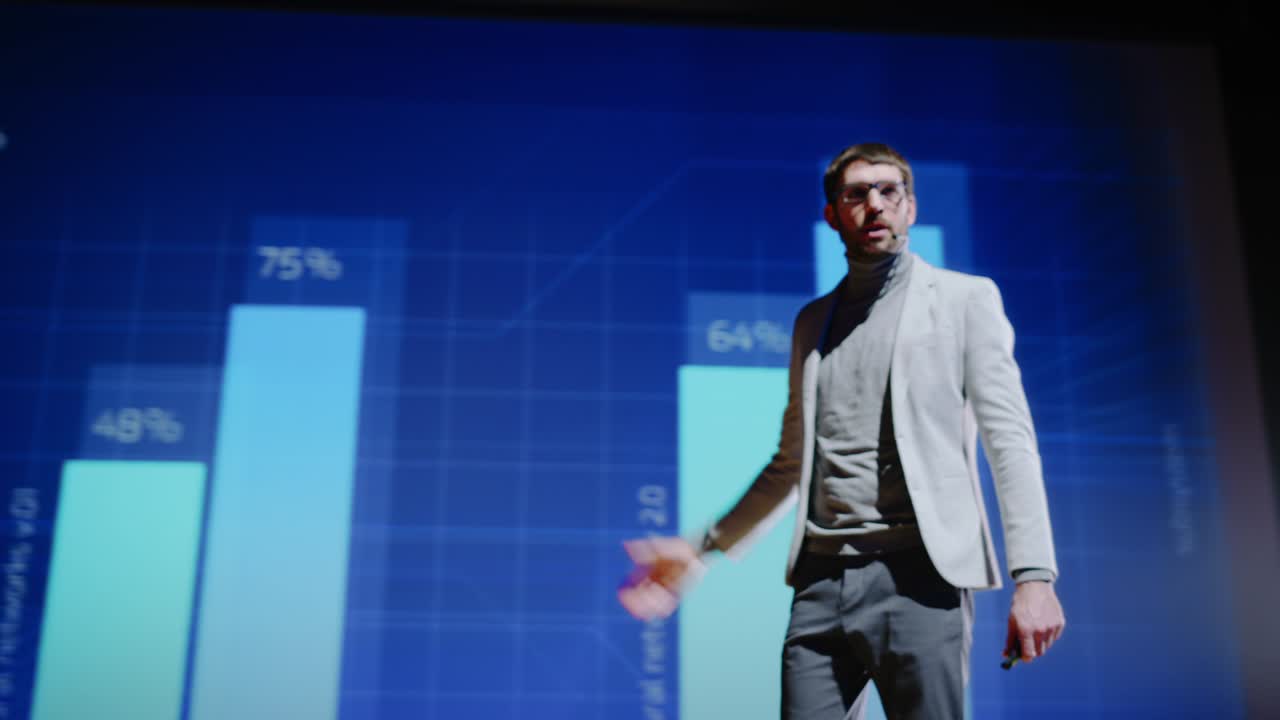 orador en el escenario saluda a la audiencia, presentación de un dispositivo tecnológico, muestra animación de infografías en la pantalla grande. evento en vivo en la sala del auditorio, lanzamiento de productos, conferencia de puesta en marcha. ángulo bajo