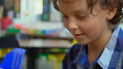 vista frontal de un escolar caucásico usando una tableta digital en el aula de la escuela 4k