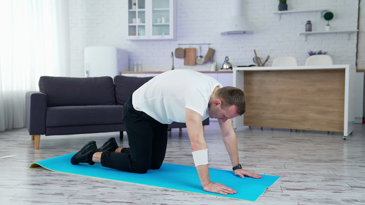 Guy doing his workout at home. Young man on a mat doing exercise of flexion and extension his back on kitchen background. Training during lockdown.