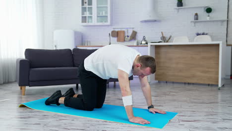 guy doing his workout at home. young man on a mat doing exercise of flexion and extension his back on kitchen background. training during lockdown.