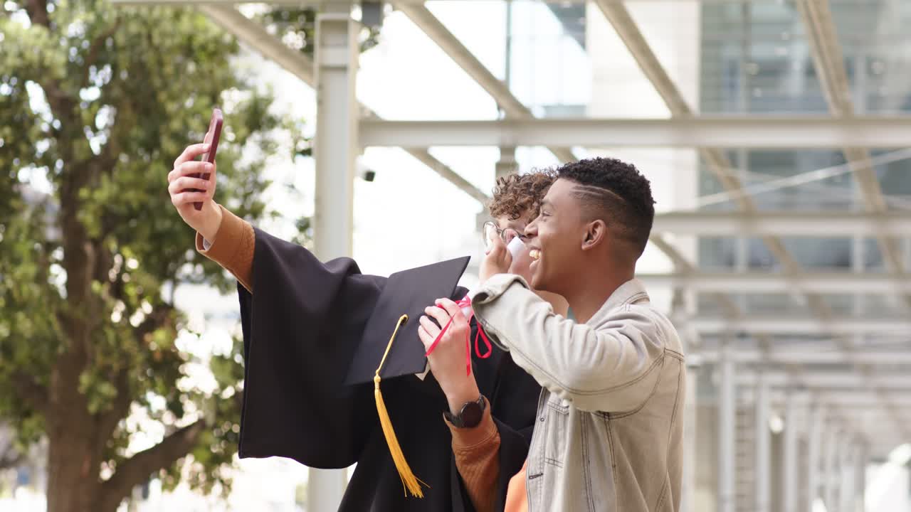 Smartphone camera activating graduate holding cap and diploma and friend waving on campus walkway