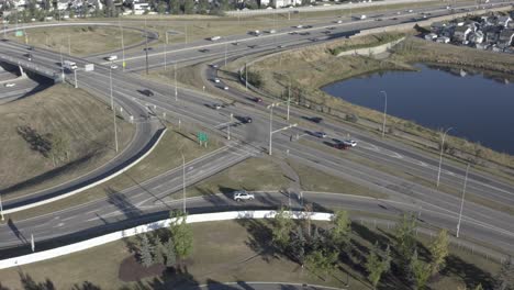 aerial early morning over sunny summer highway freeway exit enterance to the connector of the main city hub from residention to commercial avenues around cookie cut homes man made artifical pond 3-3