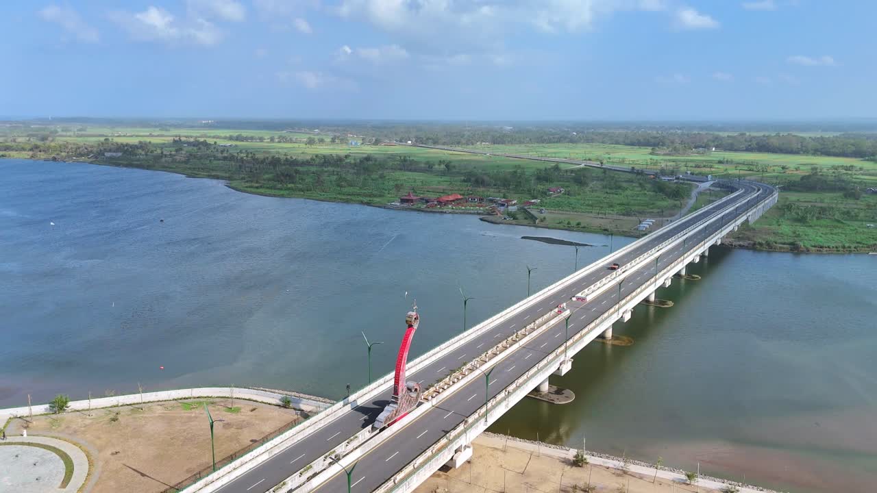 Aerial view of car vehicle crossing over bridge building on the wide river and coastline on the background and green rural landscape. Cloudy blue sky on the horizon. 4K drone footage.