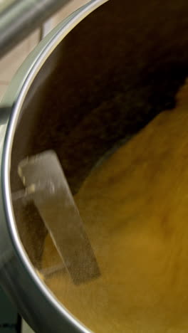 yellow substance being mixed in a big metal tank. sweet corn desserts production at the food factory. vertical video