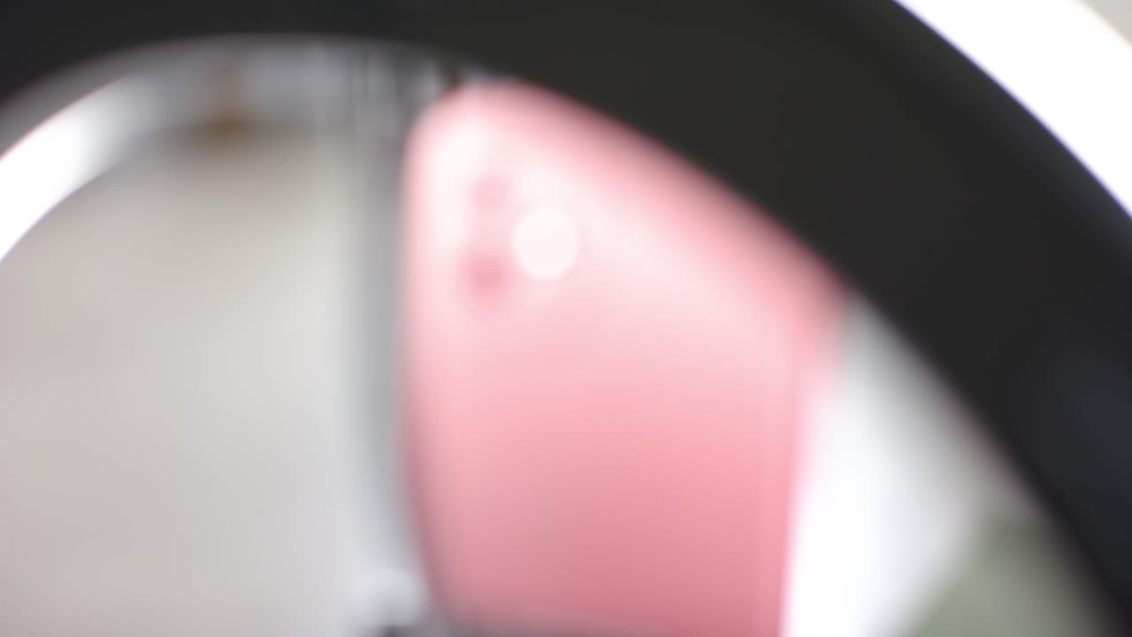 Un anello luminoso si abbassa su una bottiglia e delle cuffie, uno smartphone rosa si solleva su un supporto, mostrando delle lenti.