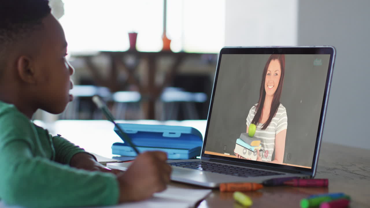 niño afroamericano haciendo la tarea mientras tiene una videollamada en una computadora portátil en casa