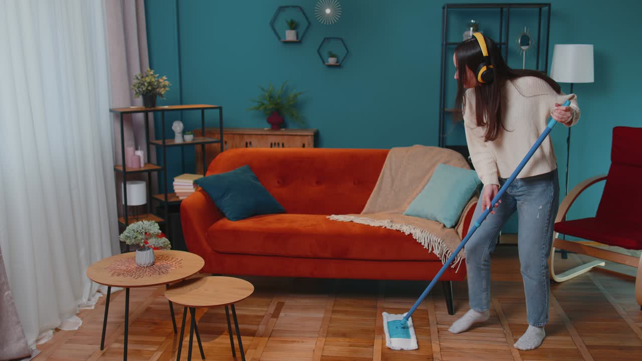 집주인 젊은 여성은 아파트 거실에서 바닥을 고 집에서 음악을 듣고 춤을 추고 있습니다.