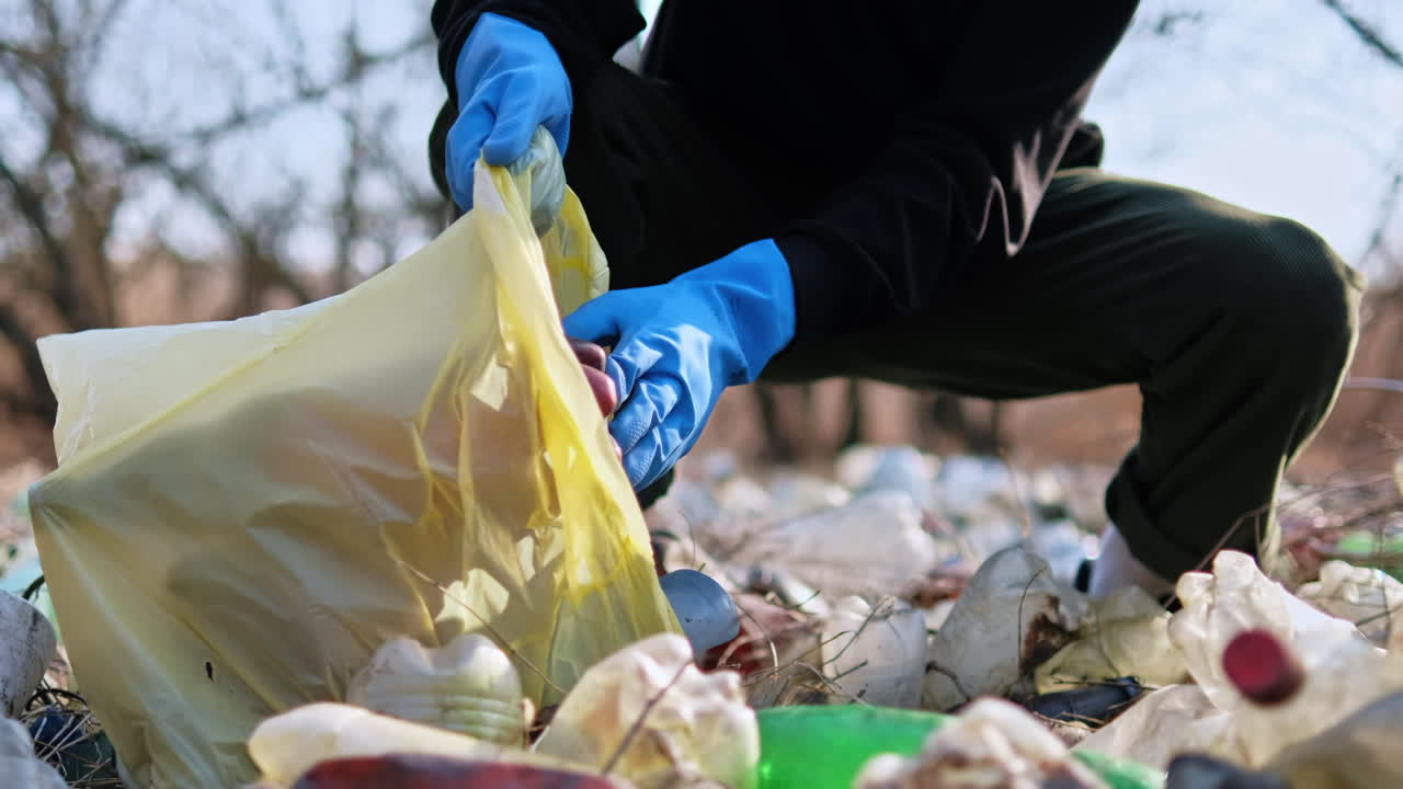 Uomo che raccoglie bottiglie di plastica sparse da terra in mezzo alla natura