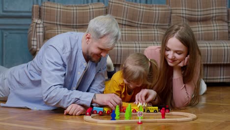 madre y padre jóvenes jugando con el niño hija montando el tren de juguete en el juego de ferrocarril de madera en casa