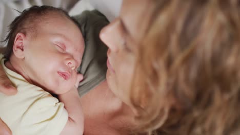 video of happy caucasian mother lying on bed with sleeping newborn baby