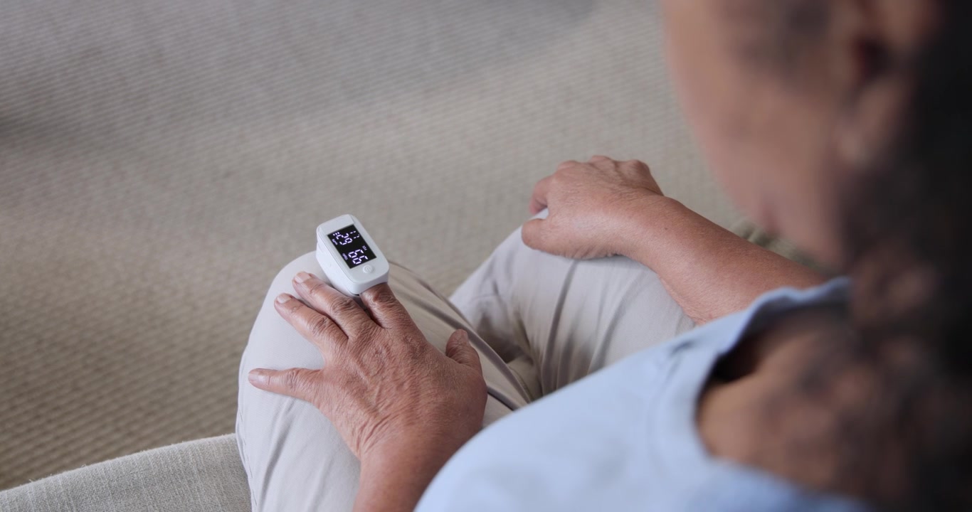 Senior African American woman seeing pulse oximeter lighting, adjusting to read on sofa, copy space