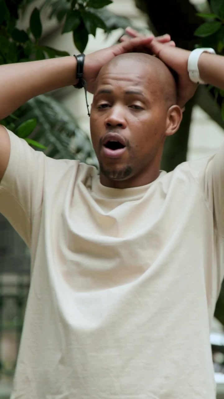 Vertical video: Talking man in tan tee pointing reacting to nearby cue checking white watch in yard