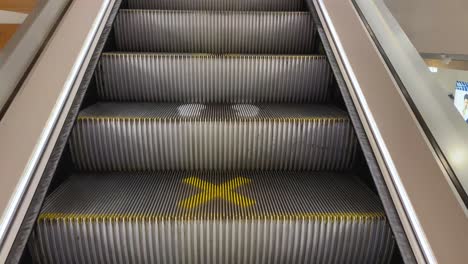 pov ascending in electric stairs at a shopping mall. social distancing signs on stairs. coronavirus pandemic