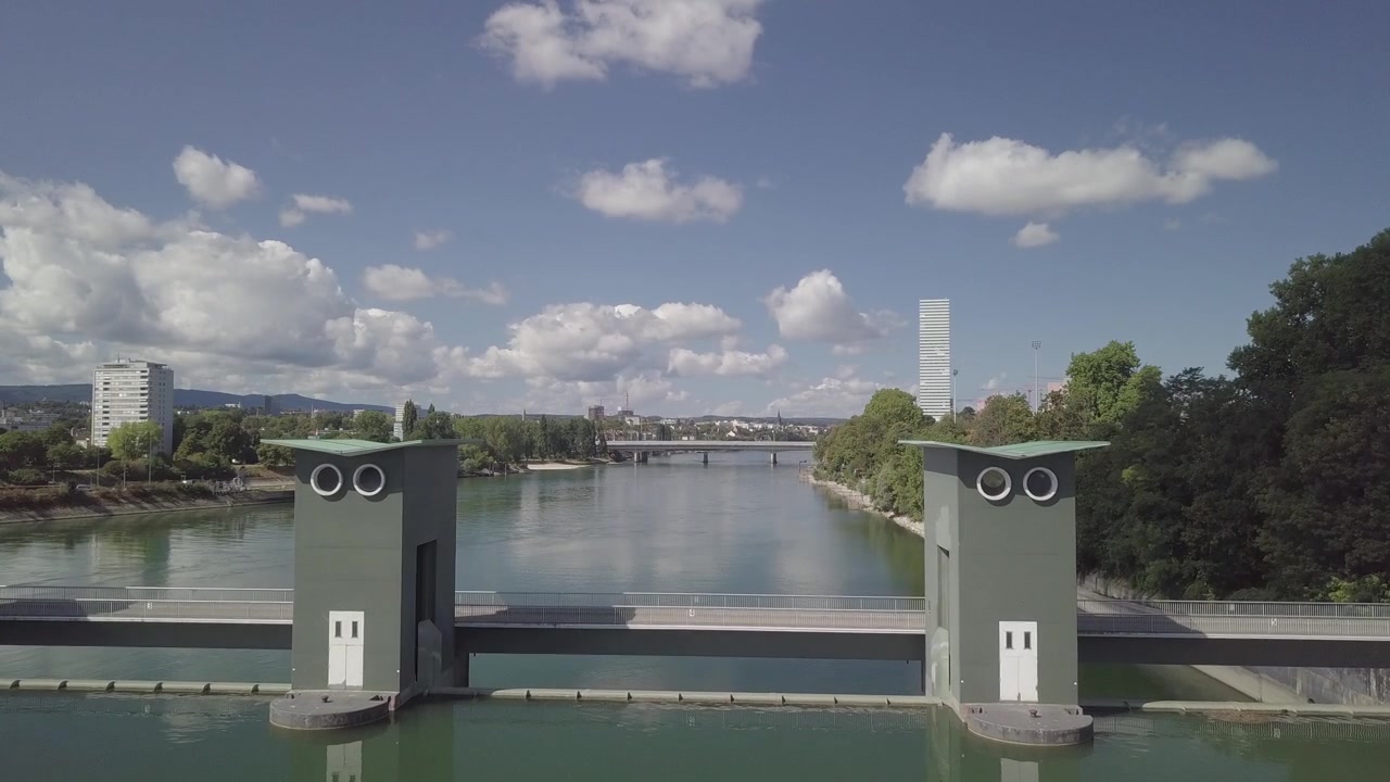Jævn droneflyvning snor sig gennem dæmningstårne med flodkanal og Roche Tower i baggrunden.