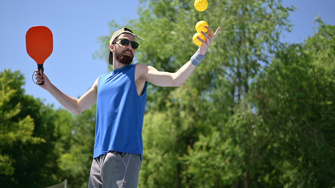 Close up of a man in a blue shirt playing pickleball with a red racket on a sunny day