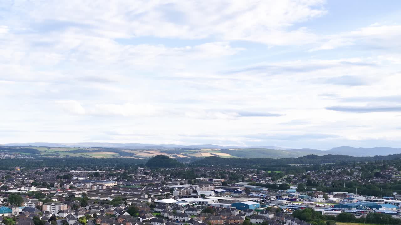 Drone pans over Dundee’s residential rooftops, revealing urban landscape, river, and distant Scottish Highlands