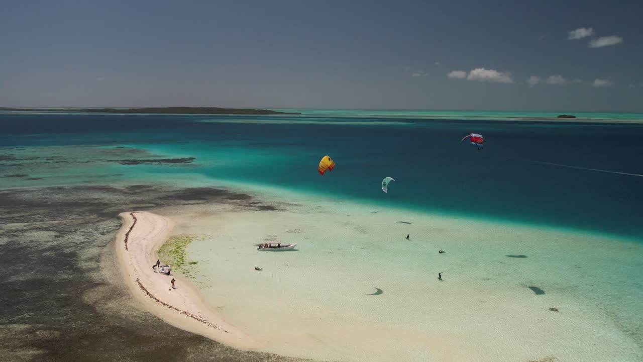 kitesurfistas deslizándose sobre aguas claras de color turquesa junto al islote de arena, los rocas, vista aérea