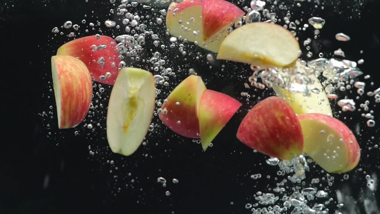 muchas piezas de manzanas maduras cayendo en el agua en el fondo negro
